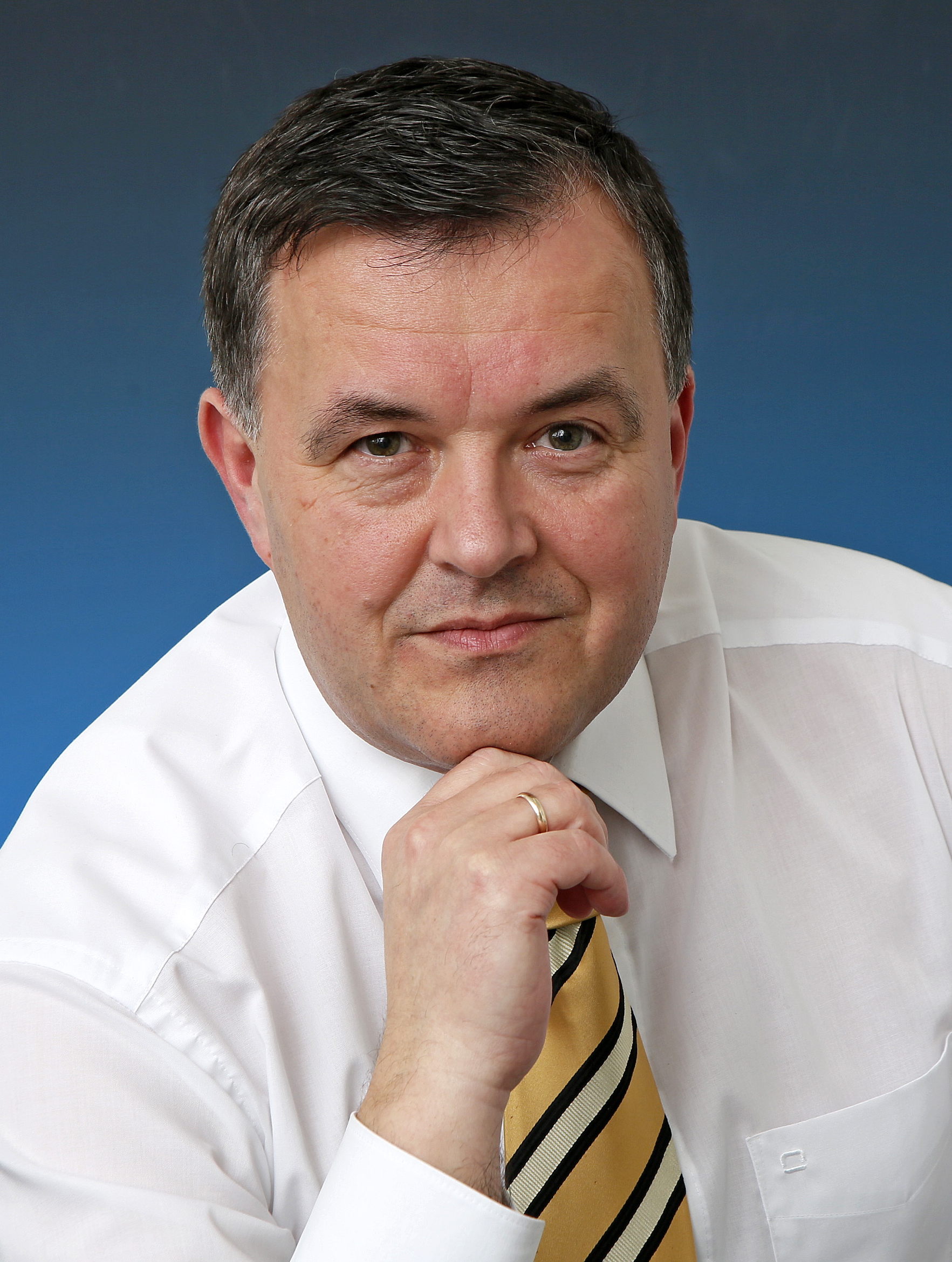 KI generiert: Das Bild zeigt einen Mann in einem weißen Hemd und einer gestreiften Krawatte, der direkt in die Kamera blickt. Er stützt sein Kinn auf seine Hand.